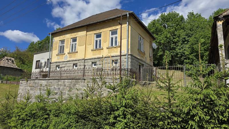 Rodinný dom v Chrťanoch s kamenným plotom, záhradou a obložená fasádou pod modrou oblohou.