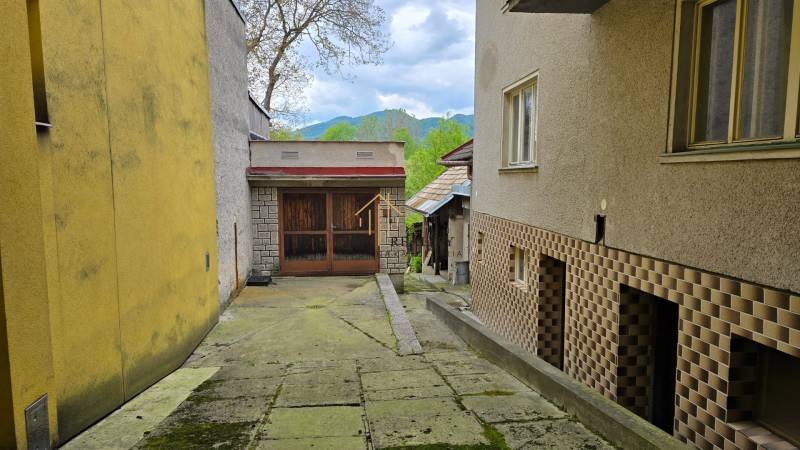 Úzky dvor v rodinnom dome v Banskej Bystrici s viditeľnými kopcami v pozadí.