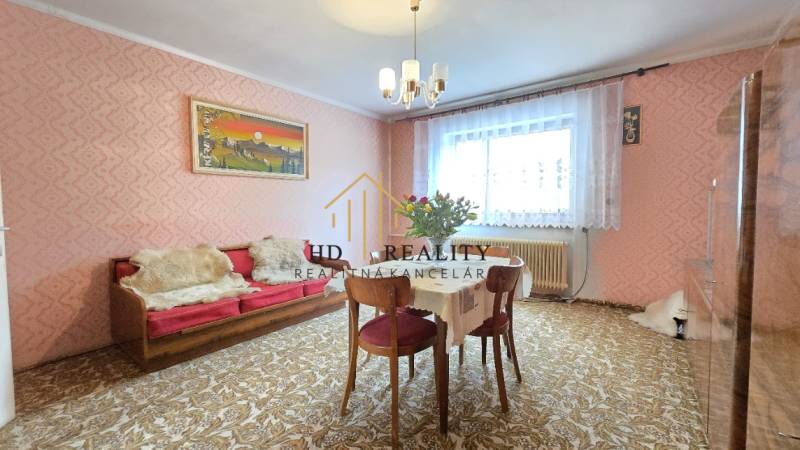 Obývacia izba s ružovými tapetami, červenou pohovkou a jedálenským stolom v rodinnom dome.