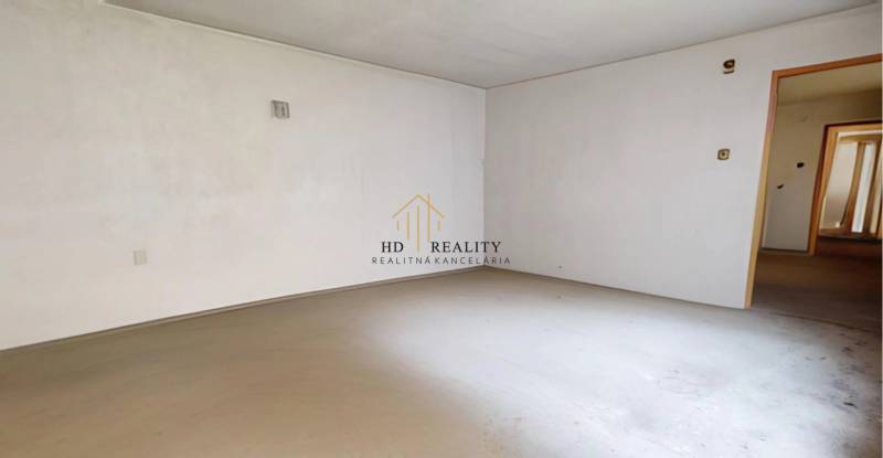 Prázdna miestnosť s bielymi stenami, betónovou podlahou a otvorenými dverami v rodinnom dome.