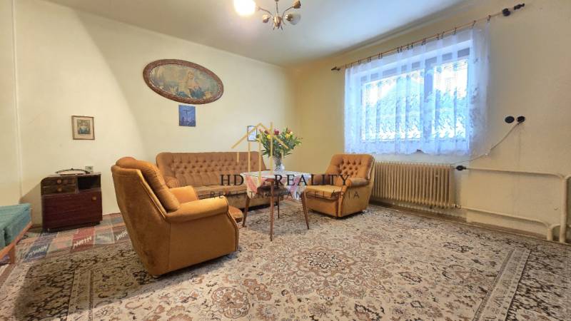 Obývačka v rodinnom dome s béžovým nábytkom, kobercom a veľkým oknom.